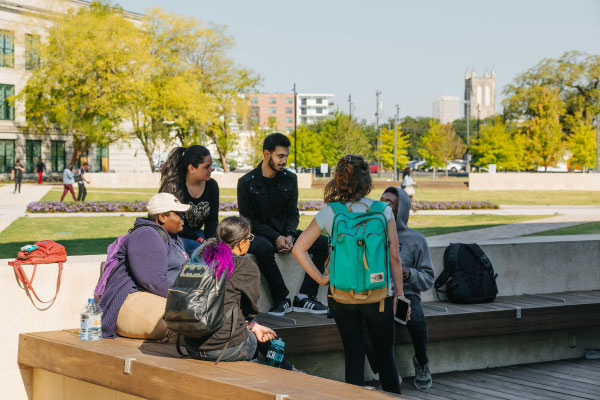 Students gathered on a bench on the lawn of the HCC Central Campus